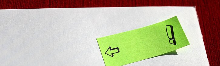 Ein Klebezettel mit einem Pfeil und einem Ausrufezeichen auf einem Blatt Papier