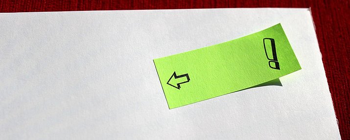 Ein Klebezettel mit einem Pfeil und einem Ausrufezeichen auf einem Blatt Papier